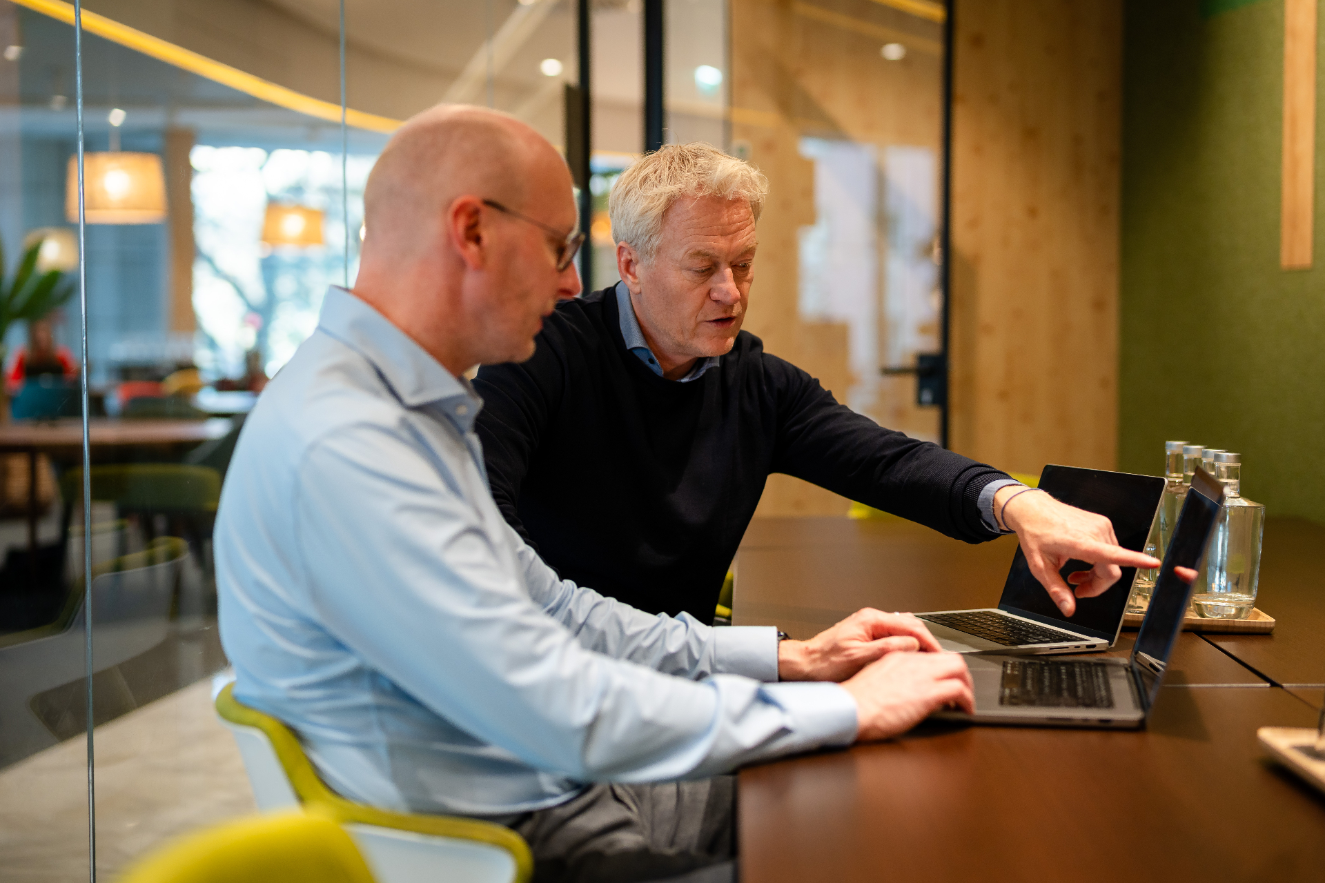 Twee Amaii oprichters in overleg aan laptops terwijl een scherm wordt aangewezen