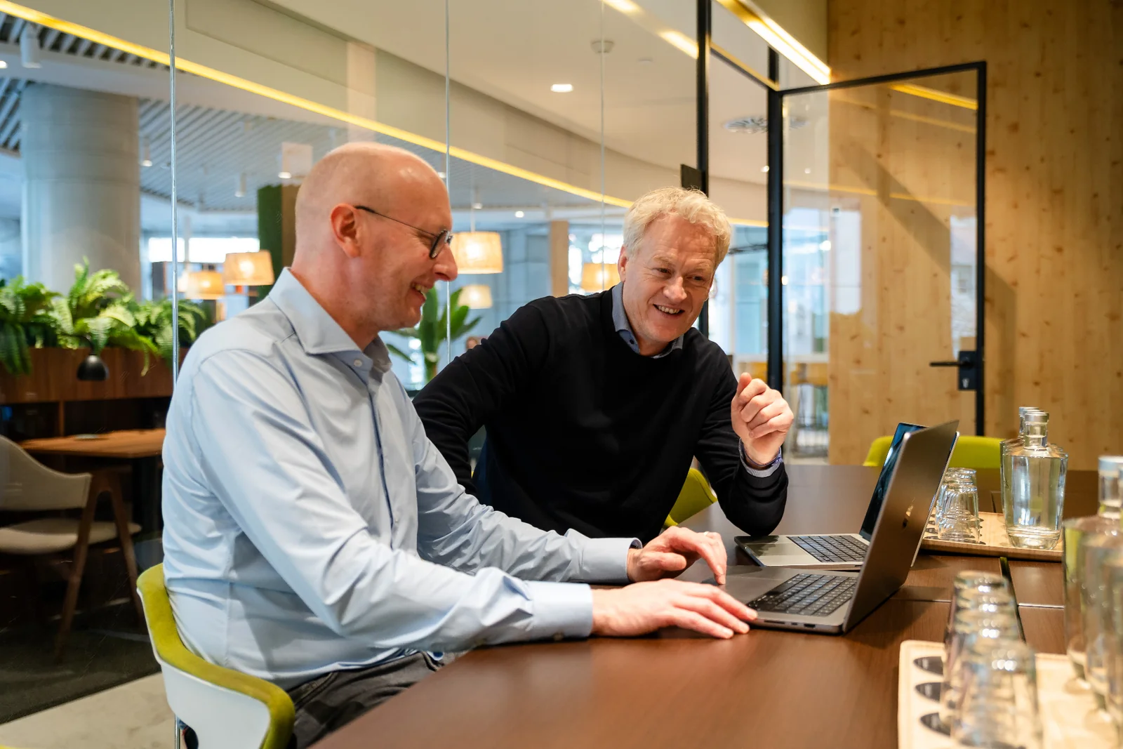 Two Amaii founders smiling while reviewing work on a laptop in a bright meeting room