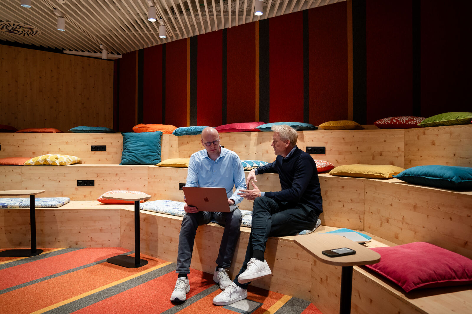 Amaii oprichters in gesprek op een houten tribune met kleurrijke kussens, een laptop op schoot