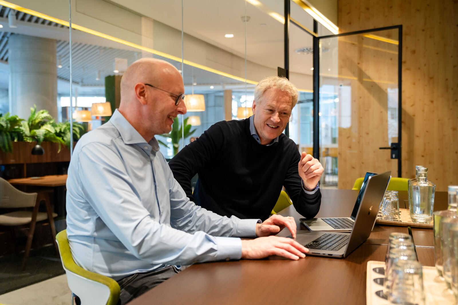 Twee Amaii oprichters lachend in overleg achter een laptop in een lichte vergaderruimte