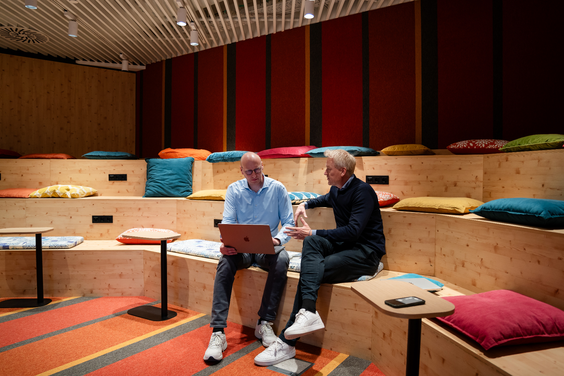 Amaii oprichters in gesprek op een houten tribune met kleurrijke kussens, een laptop op schoot